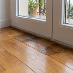Parquet in rovere con una zona scura vicino alla soglia di una portafinestra bianca con gocce sul vetro
